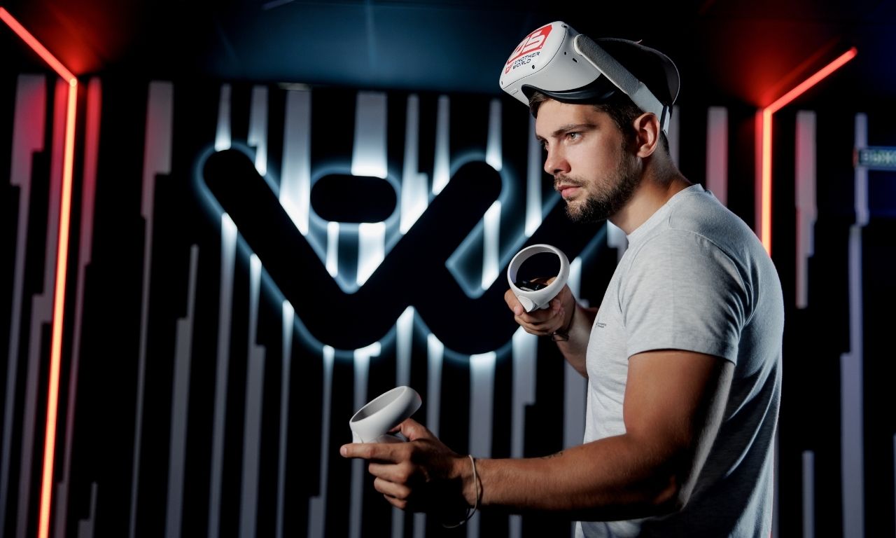 Ein Mann mit VR-Brille und Joystick steht vor dem Another World Logo